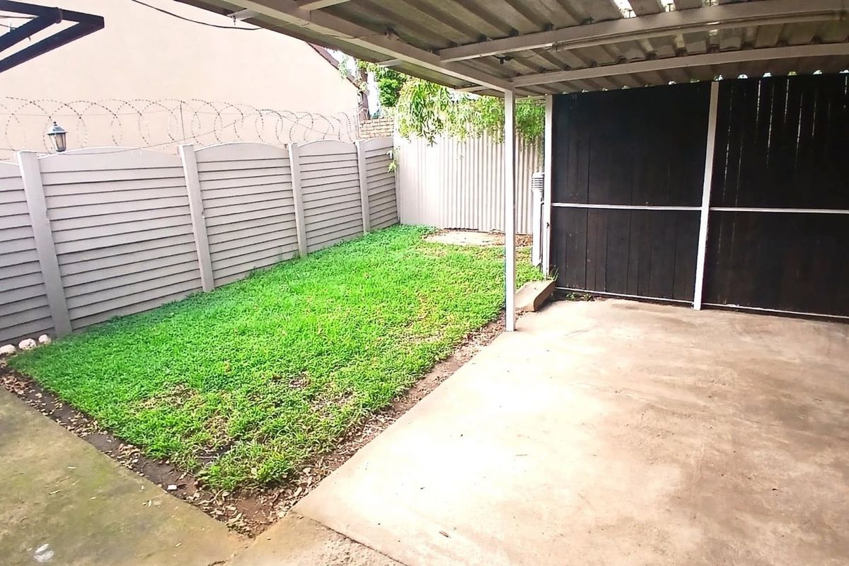 A covered outdoor patio area featuring a concrete floor, adjacent lawn space, and secure perimeter fencing with privacy screening.