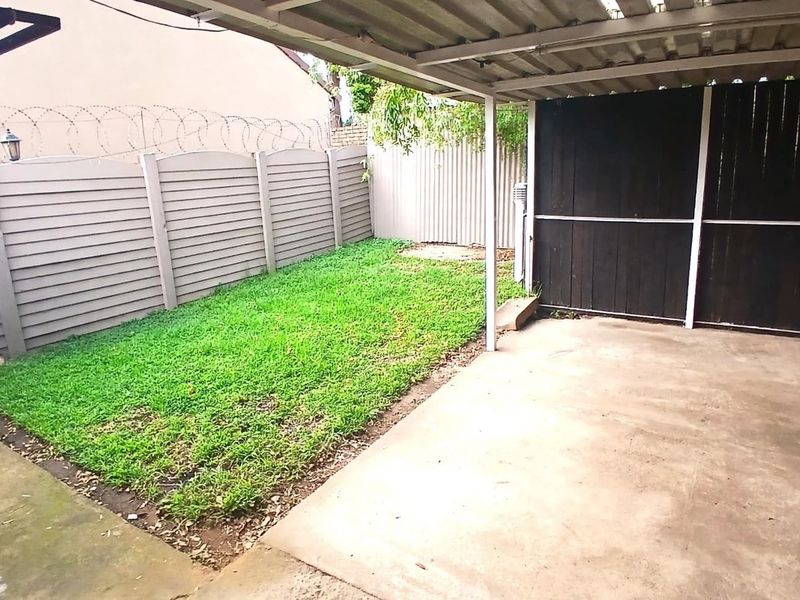 A covered outdoor patio area featuring a concrete floor, adjacent lawn space, and secure perimeter fencing with privacy screening.
