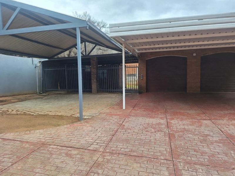 A spacious outdoor area featuring a covered carport and secure garage parking with paved driveway and steel security fencing.