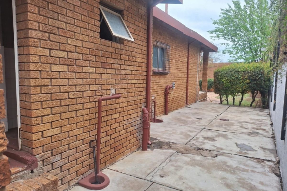 Rear exterior view of the property featuring face brick walls, concrete paving, and exposed external plumbing infrastructure.