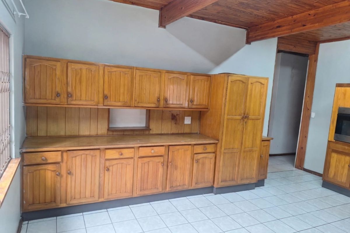 A spacious kitchen featuring extensive wooden cabinetry, tiled flooring, and exposed timber ceiling beams, offering a functional layout ready for modernization.