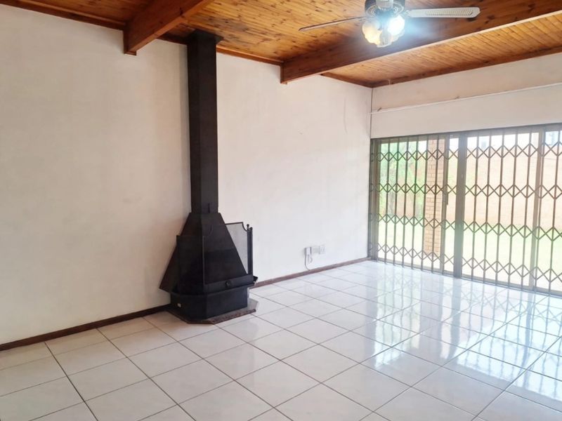 Spacious living area featuring a timber beam ceiling, ceramic floor tiles, and a freestanding fireplace, with direct access to the garden through a security gate.