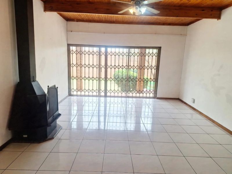 Spacious living room featuring ceramic tile flooring, an exposed timber ceiling, and a freestanding fireplace, with direct access to the garden through sliding doors.