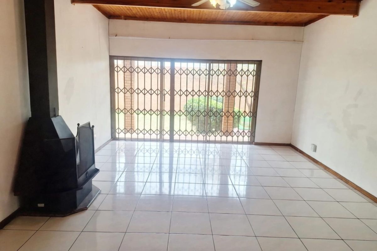 Spacious living room featuring ceramic tile flooring, an exposed timber ceiling, and a freestanding fireplace, with direct access to the garden through sliding doors.