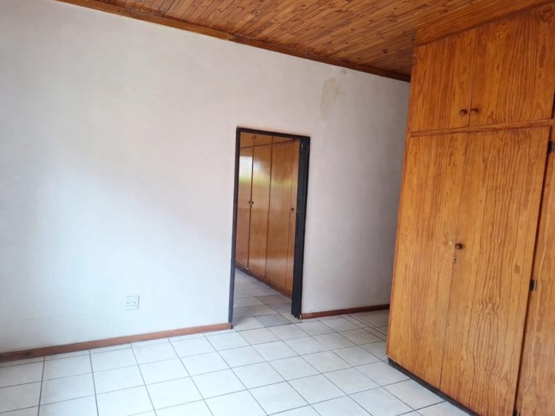 A vacant bedroom featuring tiled flooring, built-in wooden cupboards, and a wooden ceiling, requiring minor cosmetic updates to the walls.