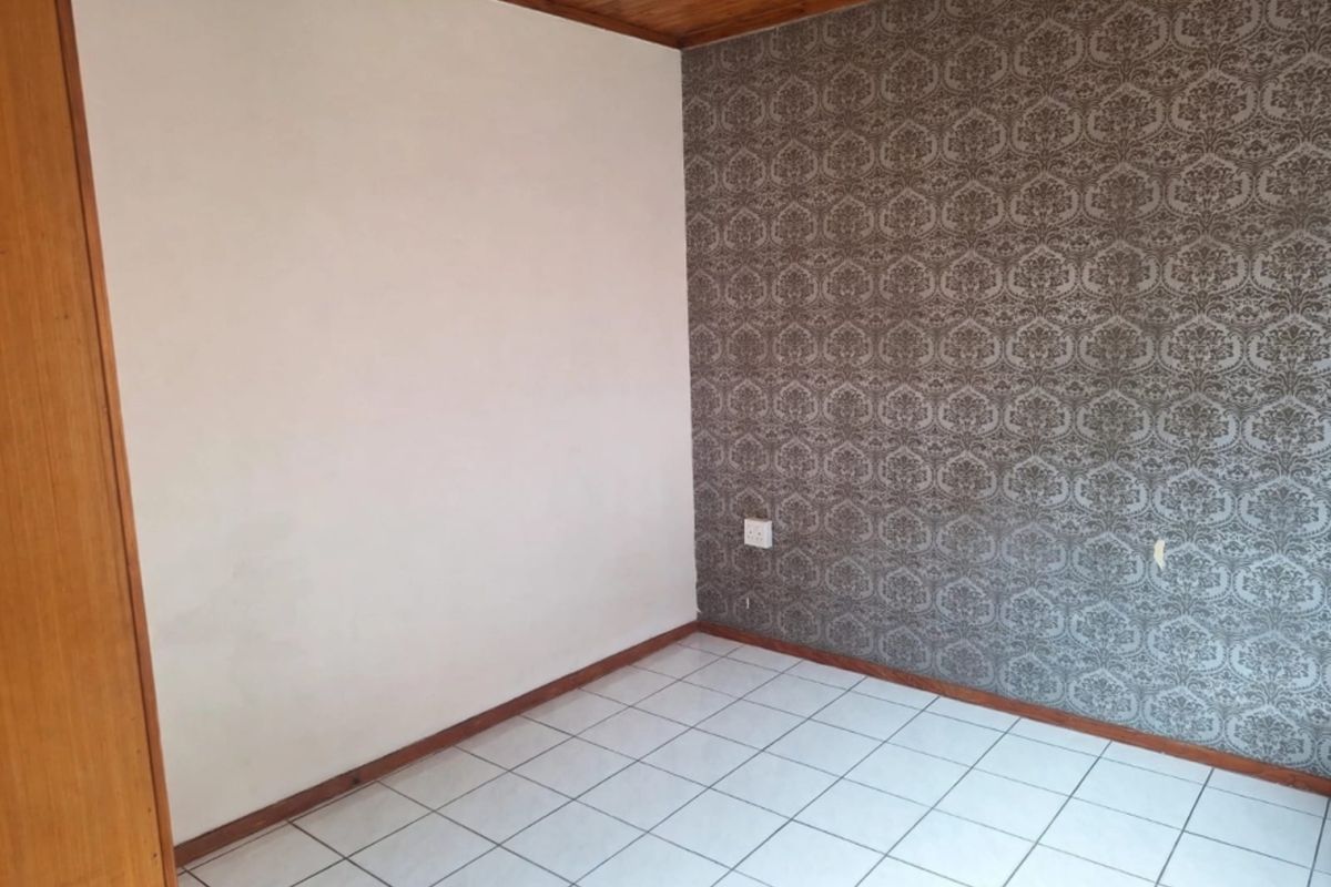An empty bedroom featuring tiled flooring, a timber ceiling, and a built-in cupboard, offering a blank canvas for potential updates.