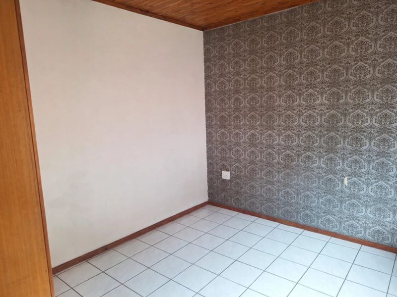 An empty bedroom featuring tiled flooring, a timber ceiling, and a built-in cupboard, offering a blank canvas for potential updates.
