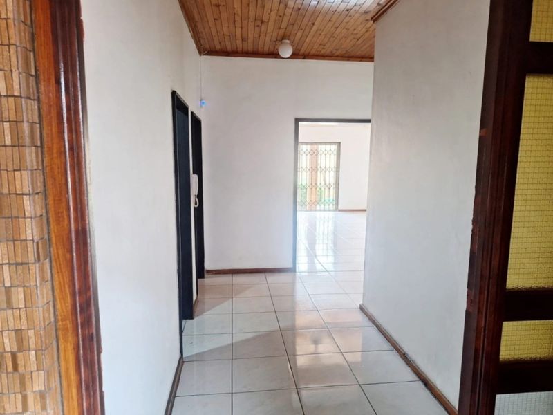 A bright, tiled hallway featuring a timber ceiling and access to adjacent living areas through a security gate.