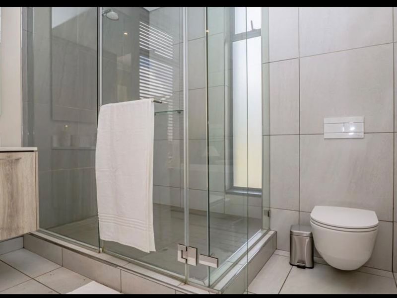 Modern bathroom featuring a glass-enclosed shower, wall-hung toilet with concealed cistern, and a contemporary vanity unit with neutral tiling.