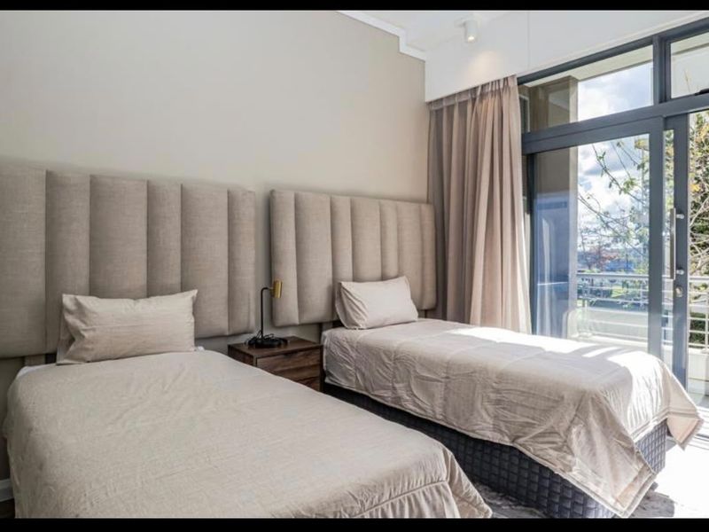 A well-lit bedroom featuring integrated upholstered headboards and a large glass sliding door providing access to an outdoor balcony area.