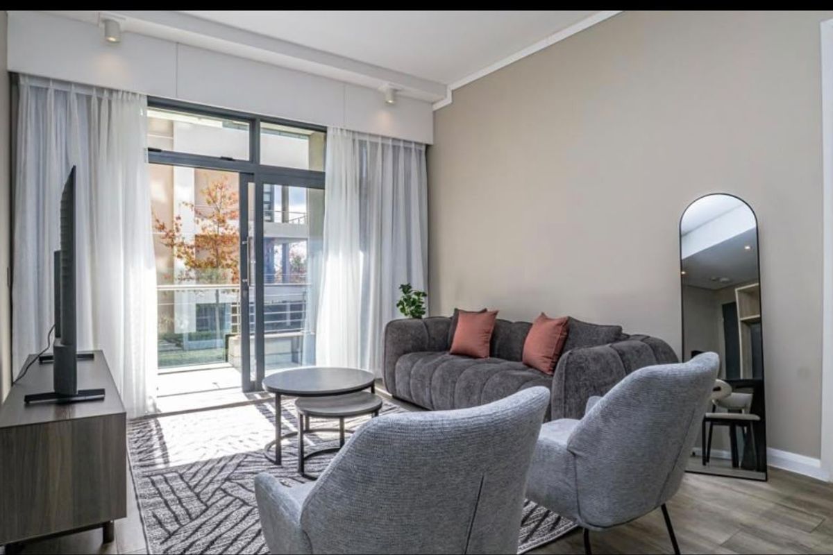 A bright and modern living room featuring laminate flooring, recessed lighting, and a large sliding glass door providing access to an outdoor balcony.