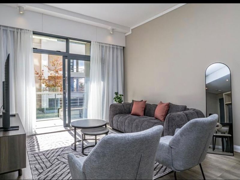 A bright and modern living room featuring laminate flooring, recessed lighting, and a large sliding glass door providing access to an outdoor balcony.
