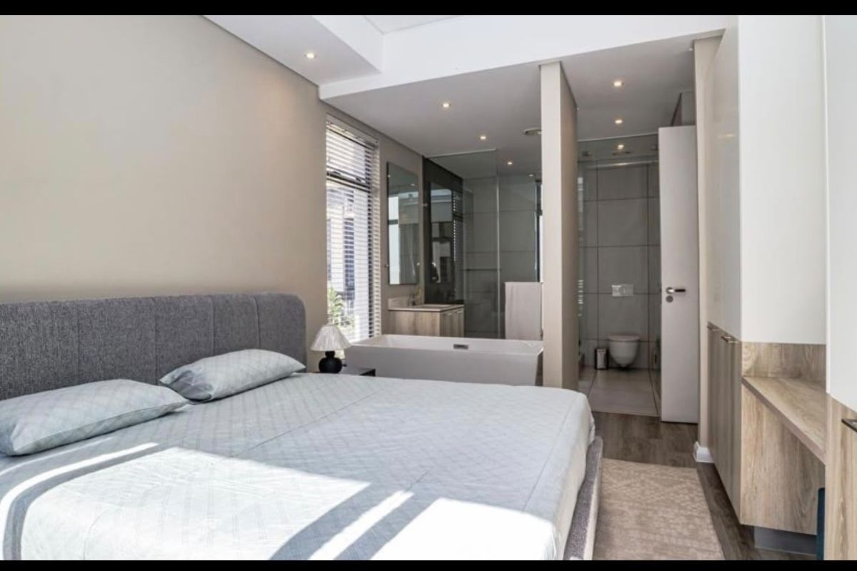 Modern bedroom featuring an open-plan en-suite bathroom with a freestanding bathtub, glass shower, and wall-hung toilet, complemented by built-in cabinetry and recessed lighting.