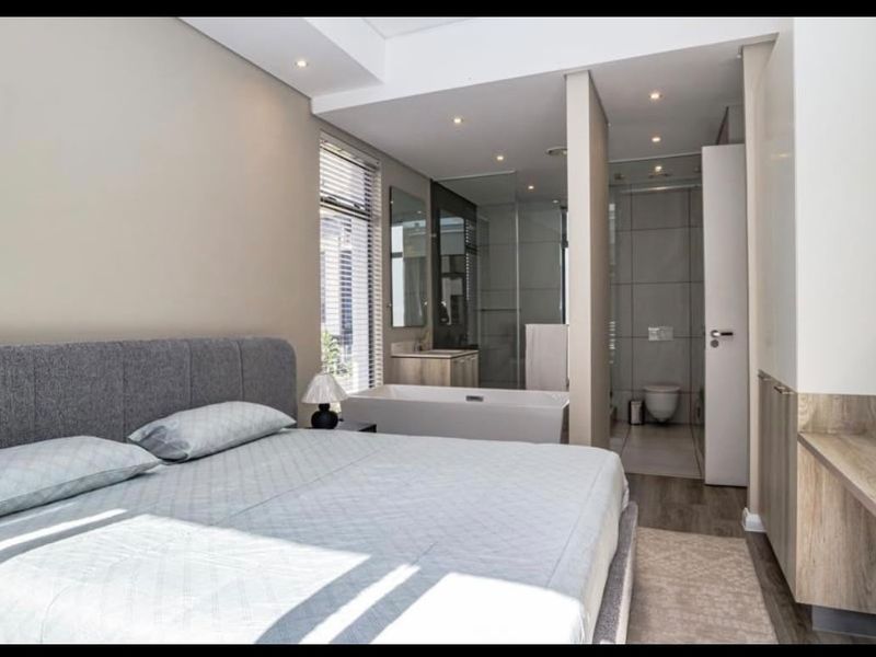 Modern bedroom featuring an open-plan en-suite bathroom with a freestanding bathtub, glass shower, and wall-hung toilet, complemented by built-in cabinetry and recessed lighting.