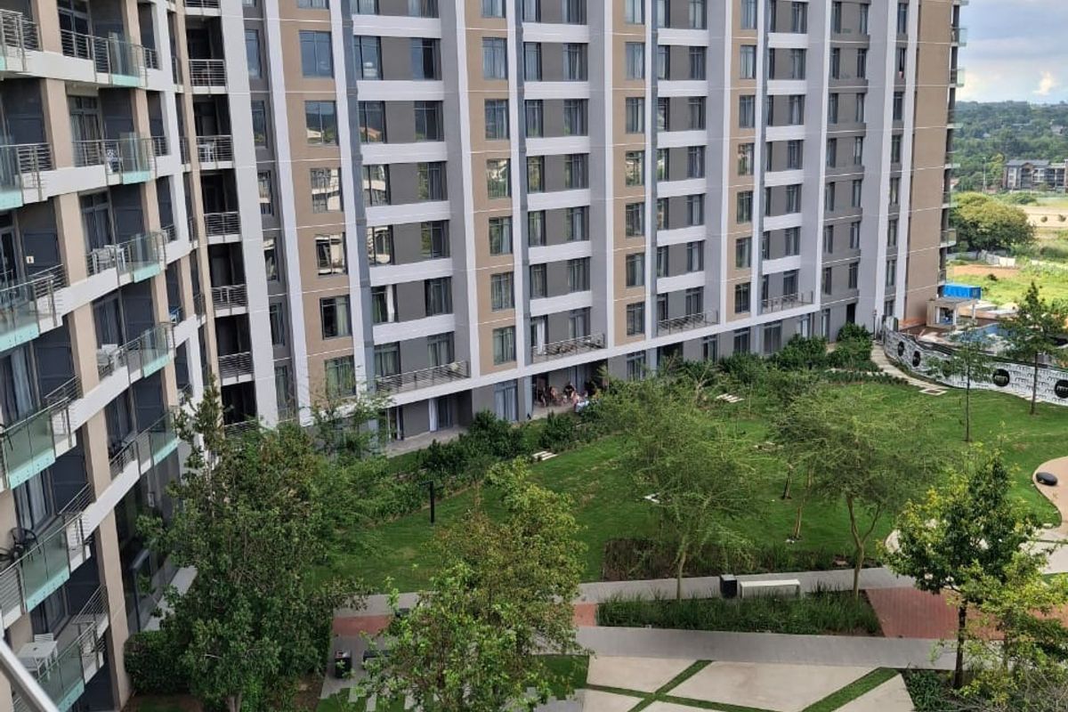 Elevated view of a modern apartment complex featuring a well-maintained landscaped garden, paved pathways, and glass-fronted balconies.