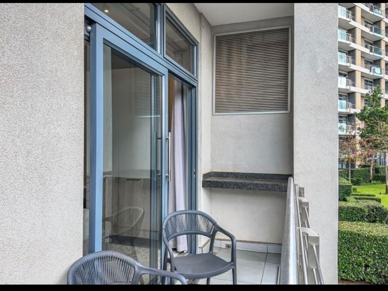 A modern apartment balcony featuring a granite shelf, sliding glass doors, and a metal balustrade overlooking the complex gardens.