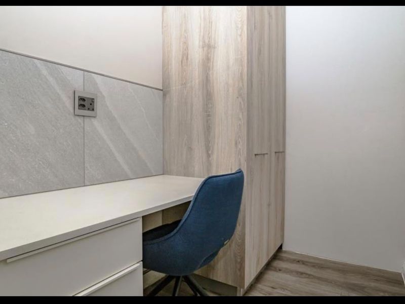 A compact, modern home office featuring a built-in desk, integrated cabinetry, and stylish stone-look wall detailing.