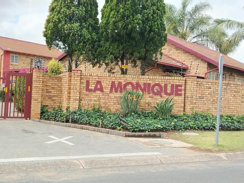 Street view of the La Monique townhouse complex entrance, featuring a brick boundary wall, electric fencing, and a secure pedestrian gate.
