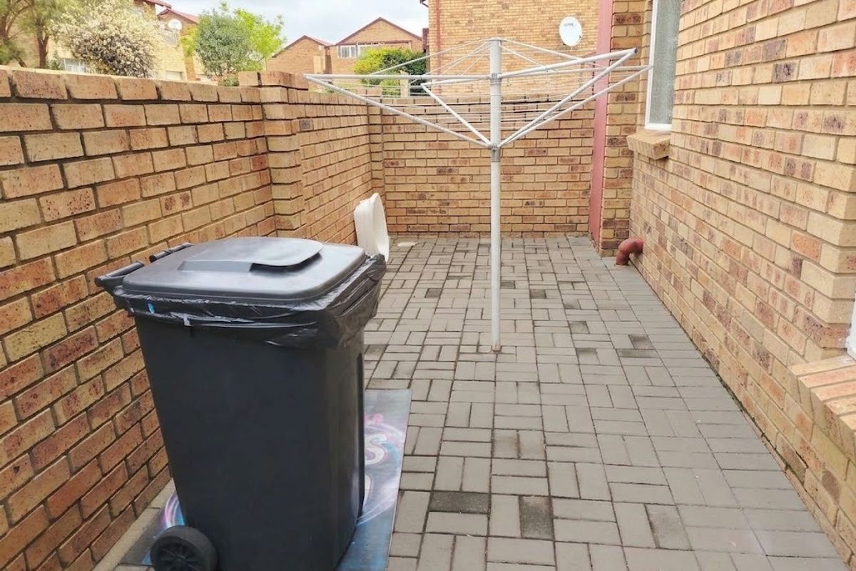 A paved rear courtyard area featuring a brick boundary wall and a fixed rotary clothesline.