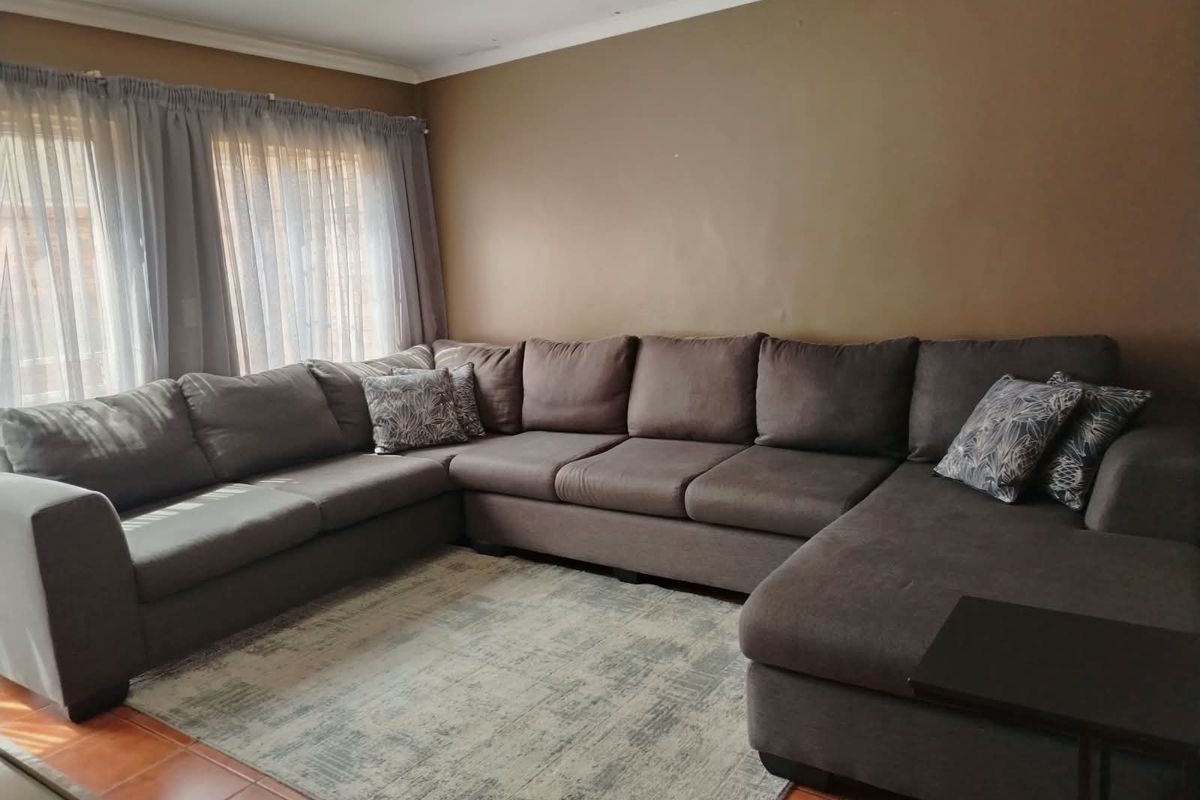 A living room featuring tiled flooring and large windows with curtain tracks, providing a functional space for relaxation.