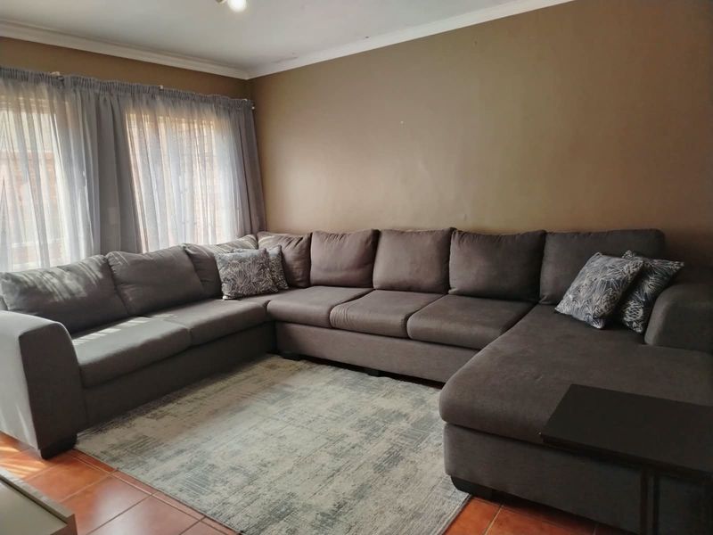 A living room featuring tiled flooring and large windows with curtain tracks, providing a functional space for relaxation.