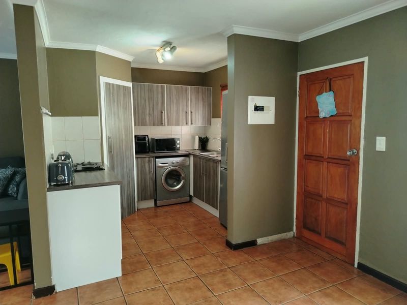 Compact kitchen featuring wood-look cabinetry, tiled flooring, built-in hob, and integrated laundry space, offering a functional layout for a townhouse.