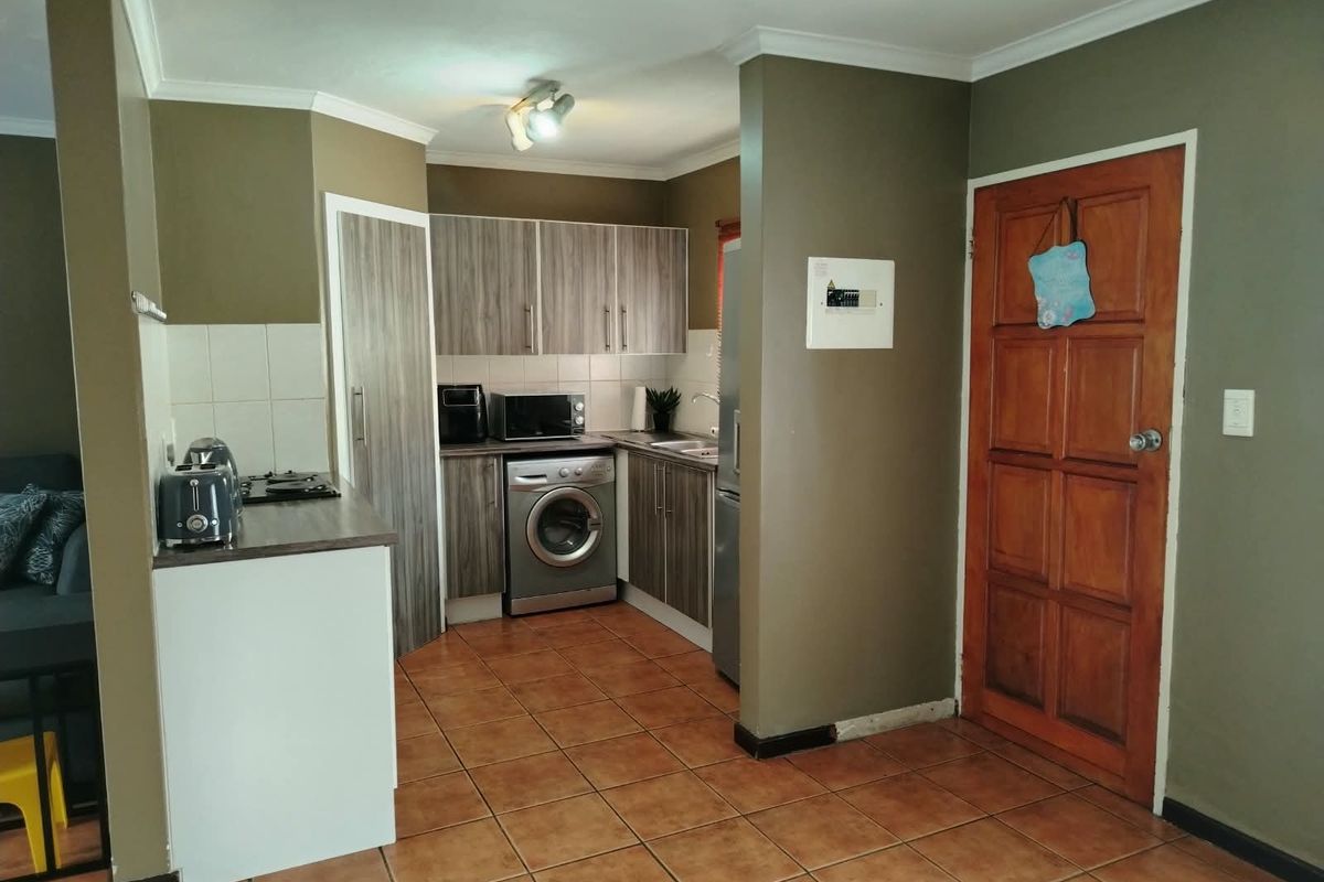 Compact kitchen featuring wood-look cabinetry, tiled flooring, built-in hob, and integrated laundry space, offering a functional layout for a townhouse.