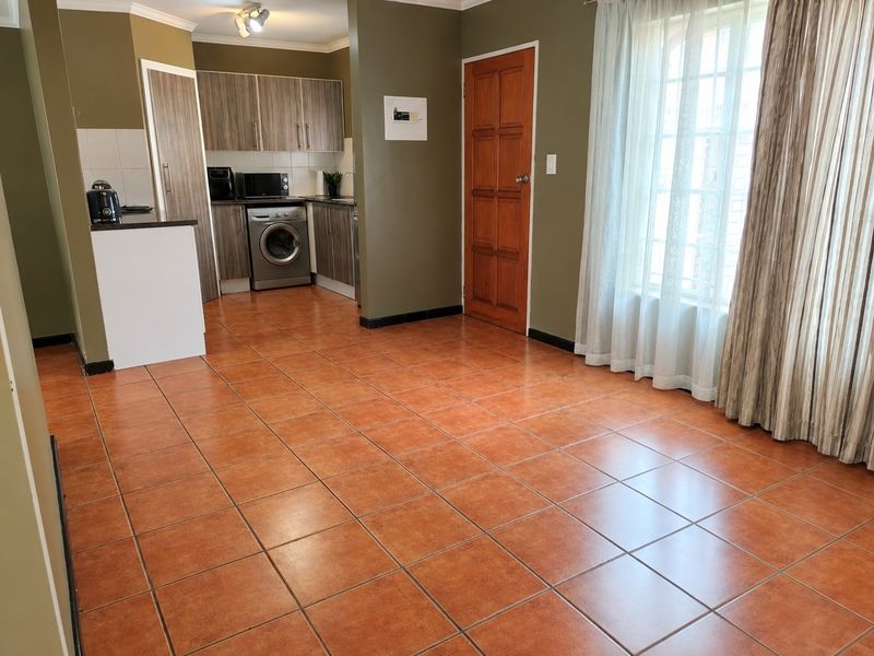Open-plan living area featuring terracotta-style floor tiles, a compact kitchen with built-in cabinetry, and direct access to a timber door.