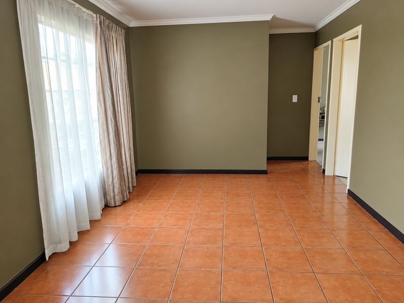 An empty living room featuring terracotta-style ceramic floor tiles, olive green walls, and white cornice detailing.