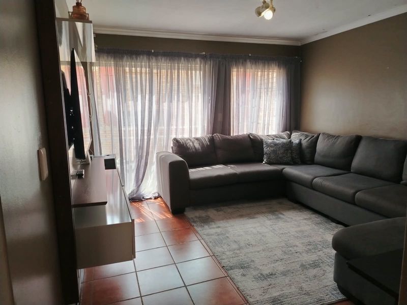 A comfortable living room featuring tiled flooring, a large sliding glass door providing natural light, and a coved ceiling.