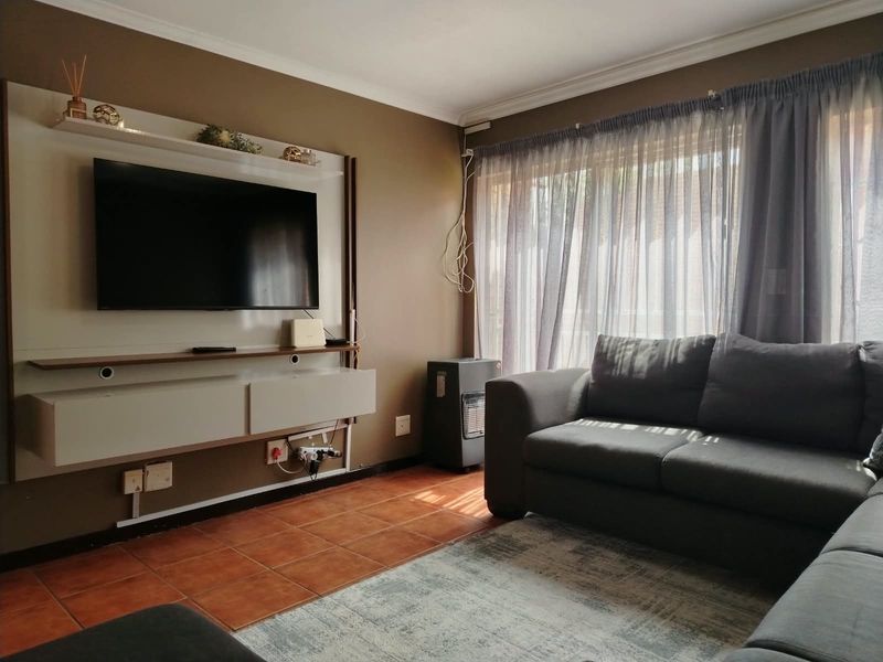 A comfortable living room featuring terracotta floor tiles, a built-in media unit, and large windows with curtain treatments.