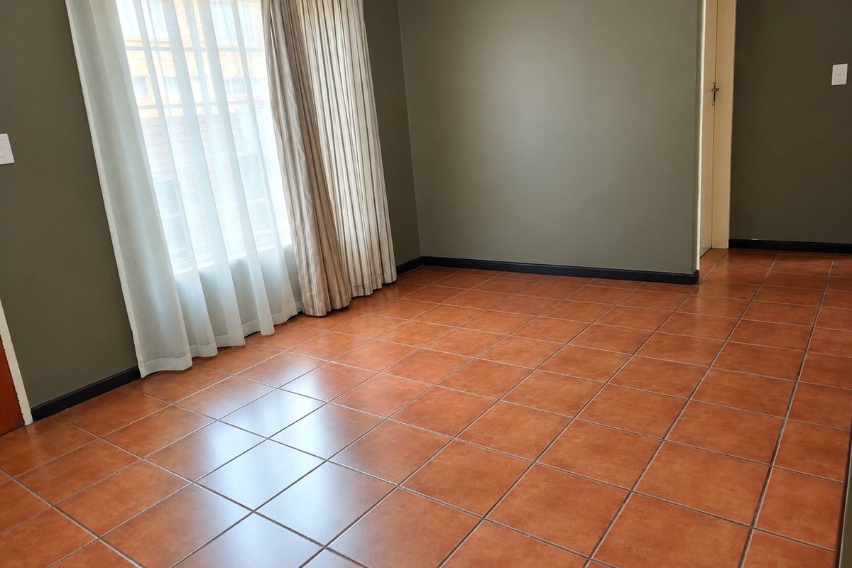 An empty bedroom featuring terracotta-style ceramic floor tiles, dark olive-toned walls, and installed curtain tracks.
