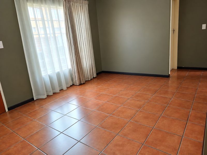 An empty bedroom featuring terracotta-style ceramic floor tiles, dark olive-toned walls, and installed curtain tracks.
