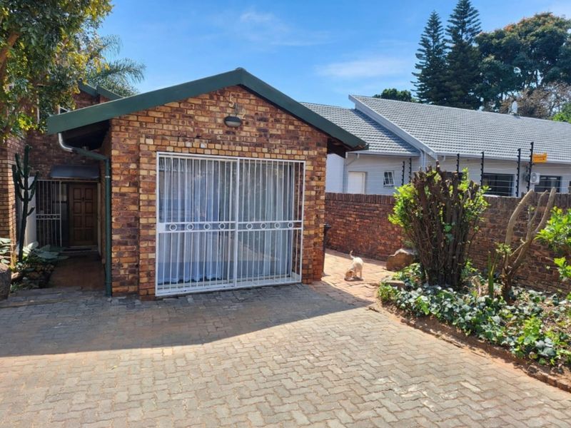 A front view of a face brick property featuring a paved driveway, secure entrance gate, and established garden boundary wall.
