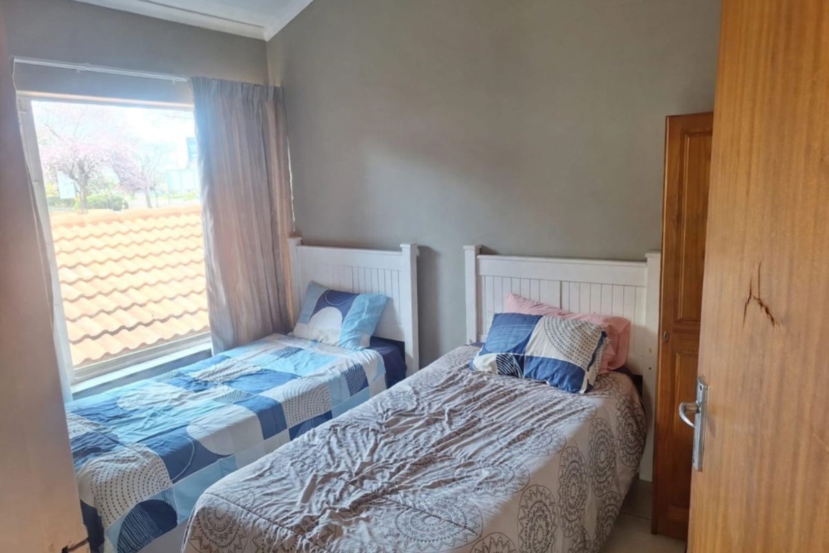 A functional bedroom featuring tiled flooring, a built-in wooden cupboard, and a large window providing natural light.