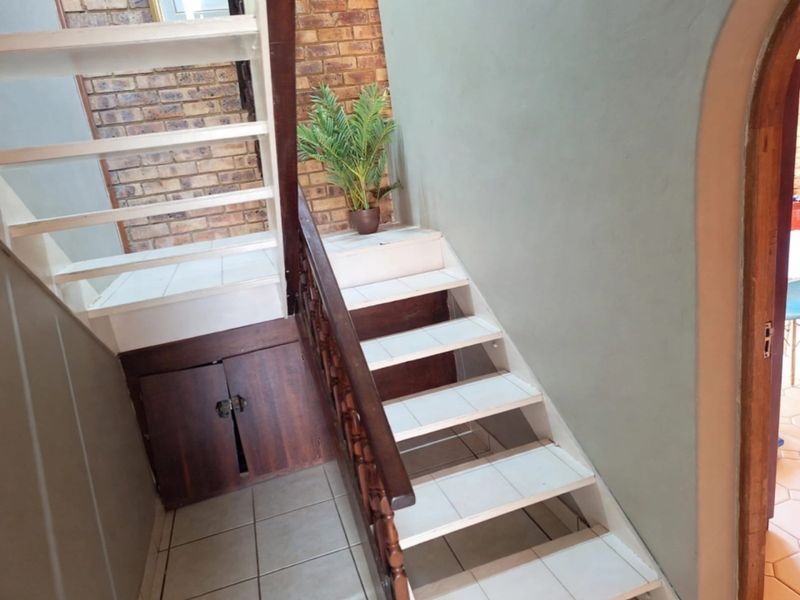 A staircase featuring tiled steps, a wooden balustrade, and built-in under-stair storage, set against an exposed brick wall.