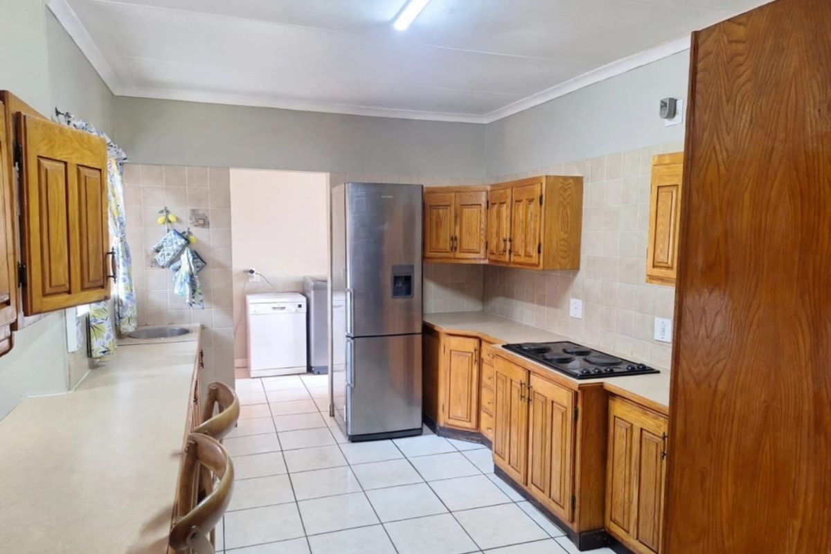 Functional kitchen featuring wooden cabinetry, laminate countertops, tiled backsplash, and a built-in electric hob, with an adjacent utility area.