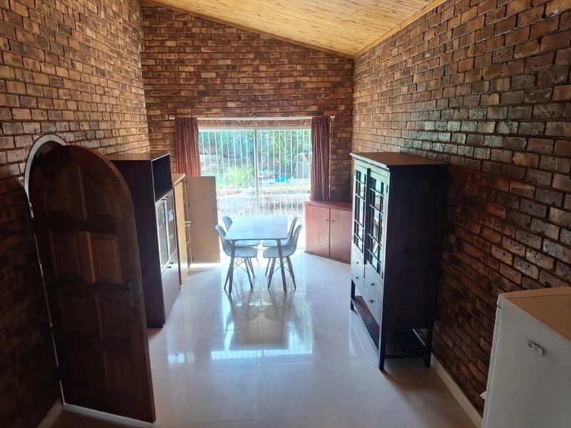 Living area featuring exposed brick walls, vaulted timber ceiling, tiled flooring, and a sliding glass door providing access to the outdoor space.