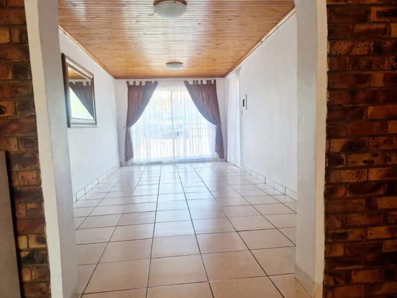 A spacious, empty living area featuring ceramic floor tiles, a timber-clad ceiling, and a sliding glass door leading to the exterior.