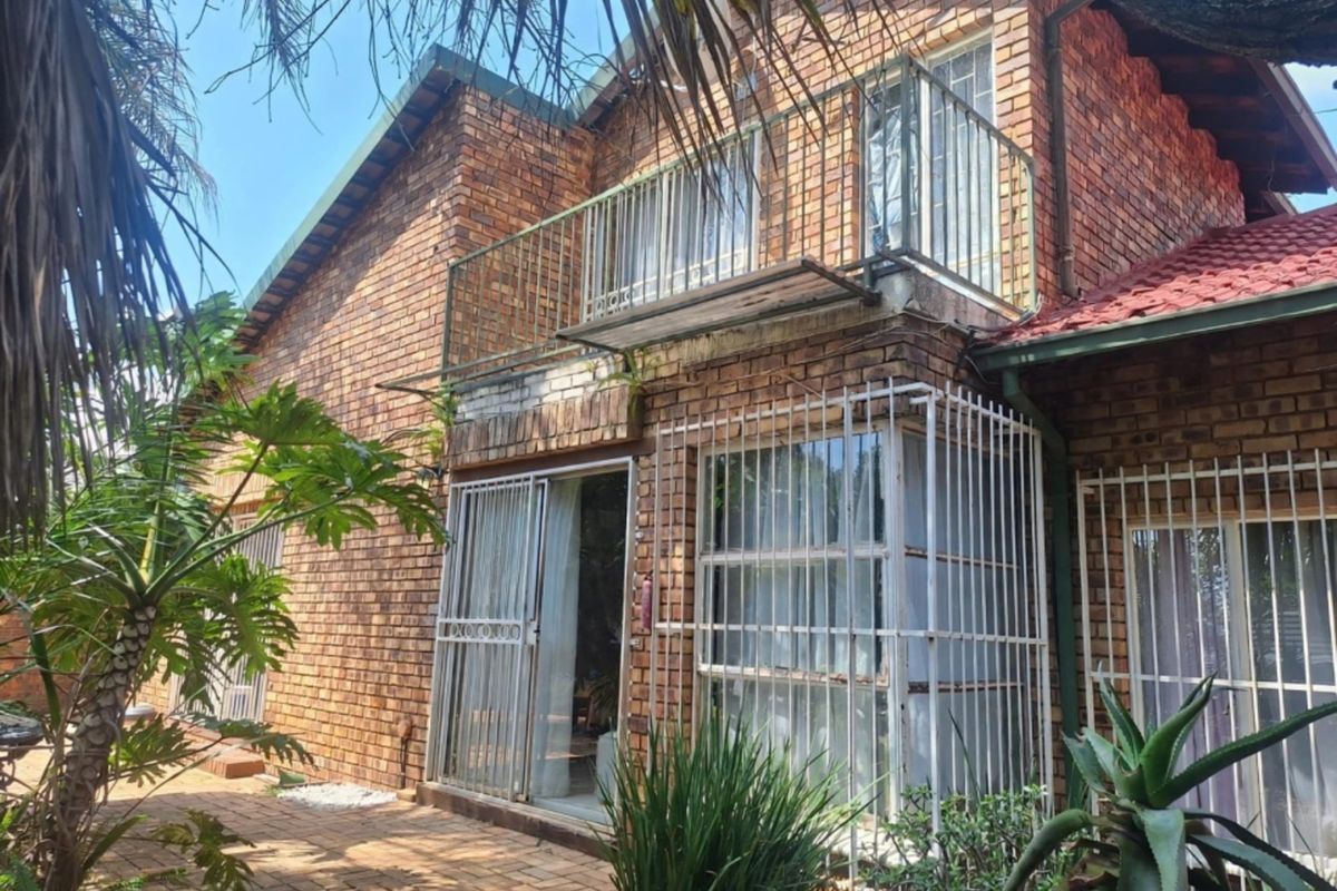 Rear view of a double-story face brick house featuring a balcony, paved patio area, and security bars on windows and doors.