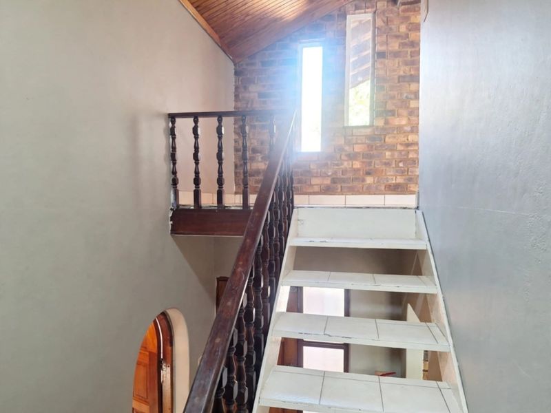 A hallway featuring a timber staircase with a traditional balustrade, exposed brick wall, and a raked timber ceiling.
