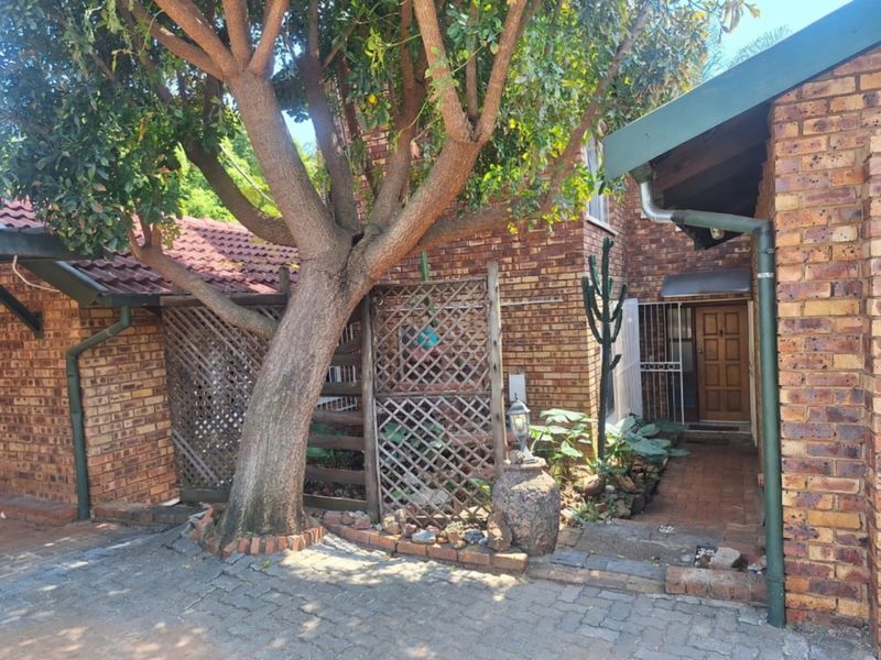 Front entrance area featuring a face brick facade, paved driveway, and established tree, providing a classic and textured exterior aesthetic.