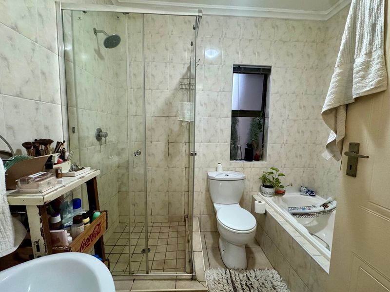 A functional bathroom featuring a glass-enclosed shower, a built-in bathtub, and a toilet, finished with neutral wall and floor tiling.