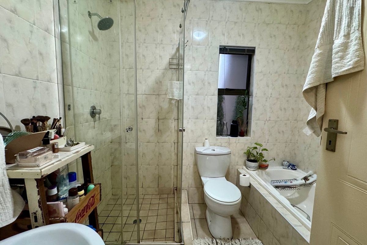 A functional bathroom featuring a glass-enclosed shower, a built-in bathtub, and a toilet, finished with neutral wall and floor tiling.