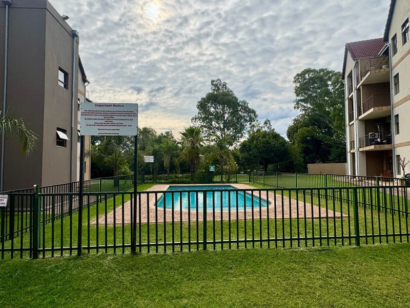 A communal swimming pool area situated between apartment blocks, featuring paved surrounds and secure metal perimeter fencing.