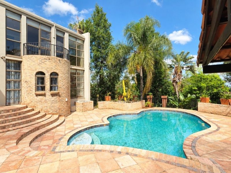 A spacious outdoor pool area featuring a curved brick staircase, paved patio, and a multi-story residence with large glass windows and a balcony.