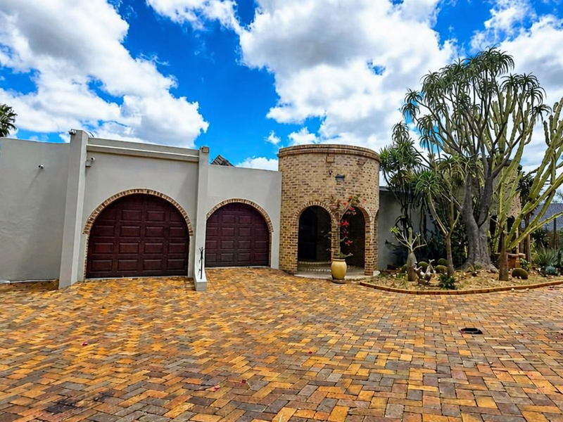 Front elevation featuring a double garage with arched doors, a distinctive brick turret entrance, and a spacious brick-paved driveway.