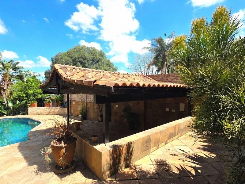 Outdoor entertainment area featuring a covered patio with terracotta roof tiles, stone wall finishes, and an adjacent swimming pool in a landscaped garden setting.