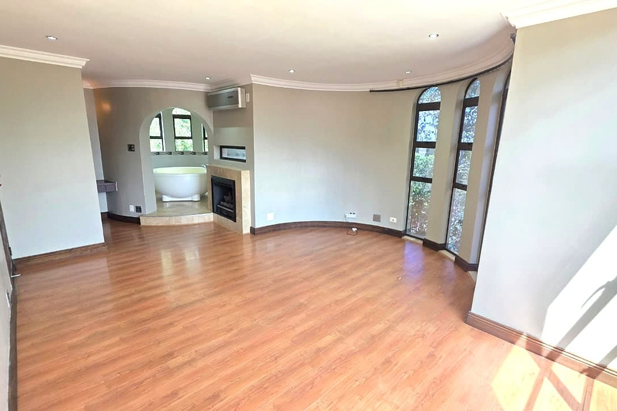 Spacious bedroom featuring laminate flooring, an integrated fireplace, and an open-plan en-suite area with a freestanding bathtub and arched windows.