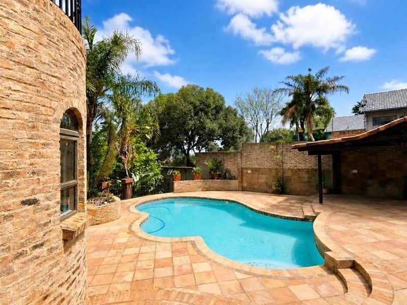 Outdoor pool area featuring a curved swimming pool, tiled patio surround, and a covered entertainment space with stone-clad architectural details.
